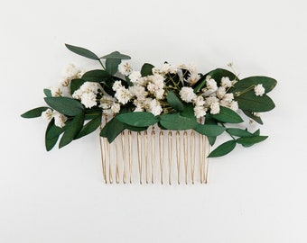 May include: A gold hair comb with white baby's breath and green eucalyptus leaves.