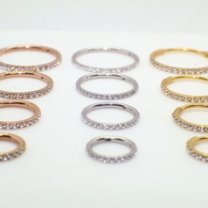 May include: A set of nine jeweled body rings in three different metal finishes: gold, silver, and rose gold. Each ring is adorned with a row of sparkling clear rhinestones.