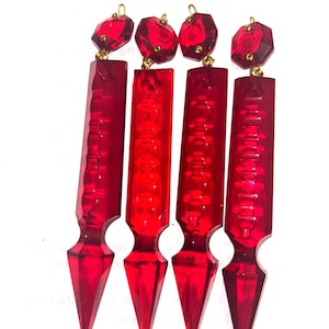 以下が含まれることがあります： ゴールドカラーのフックが付いた、赤いアクリル製のイヤリング4つ。各イヤリングは、ファセット加工された宝石のような上部と、先のとがった底を持つ長方形のボディが特徴です。イヤリングは鮮やかで透明感のある赤色です。