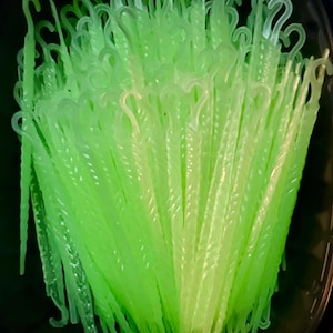 May include: A collection of numerous translucent, light green plastic ornament hooks. Each hook features a slender, elongated body with a spiral-textured design and a curved top loop for hanging. The hooks are bundled together in a dark container.