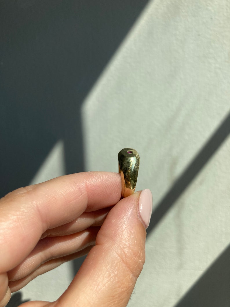 May include: A gold signet ring with a small, round, pink gemstone set in the center.