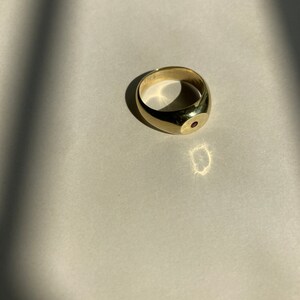 May include: A gold signet ring with a single red gemstone set in the center.