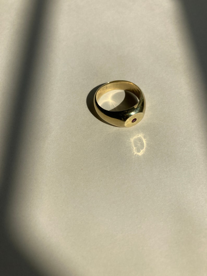 May include: A gold signet ring with a single red gemstone set in the center.