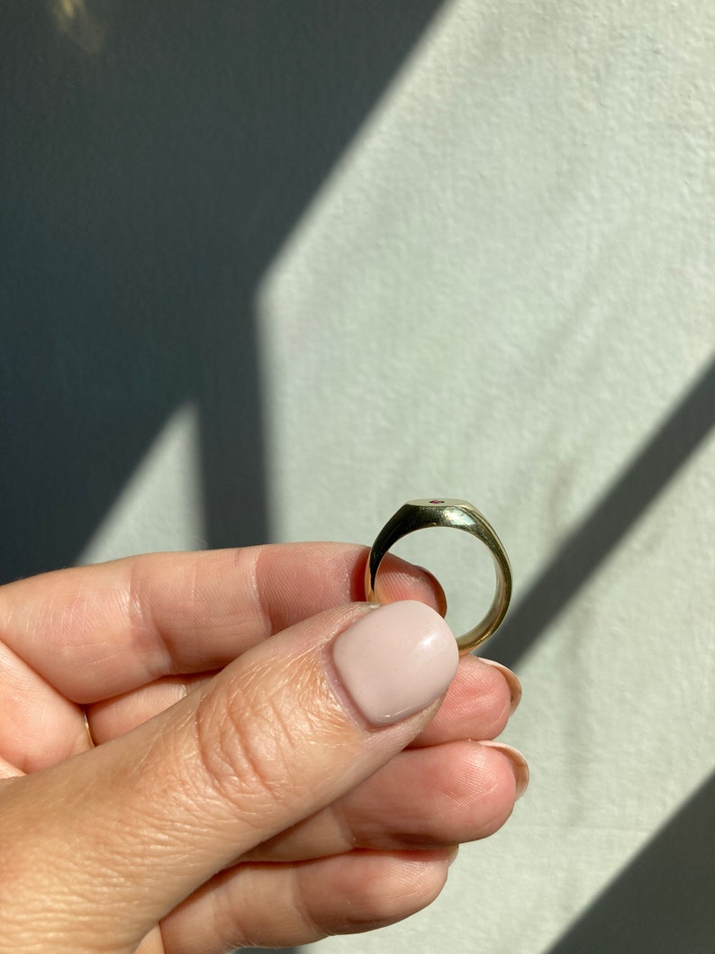 May include: A gold signet ring with a red gemstone set in the center.