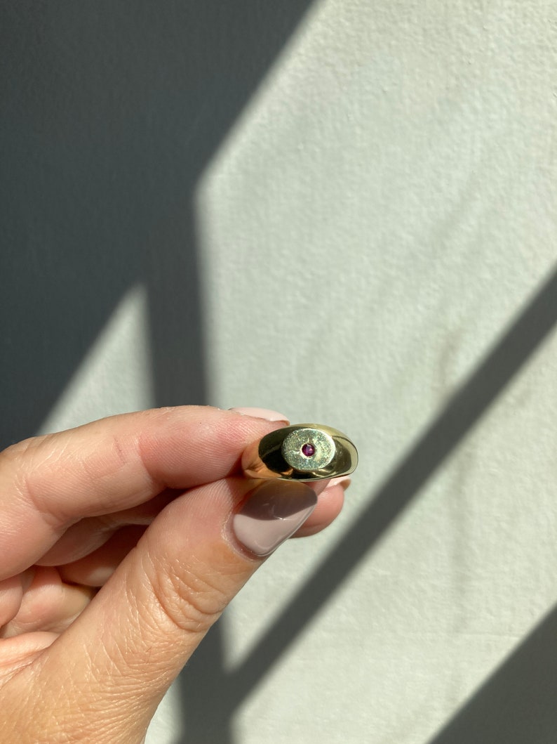 May include: A gold ring with a small, round, pink gemstone set in the center.