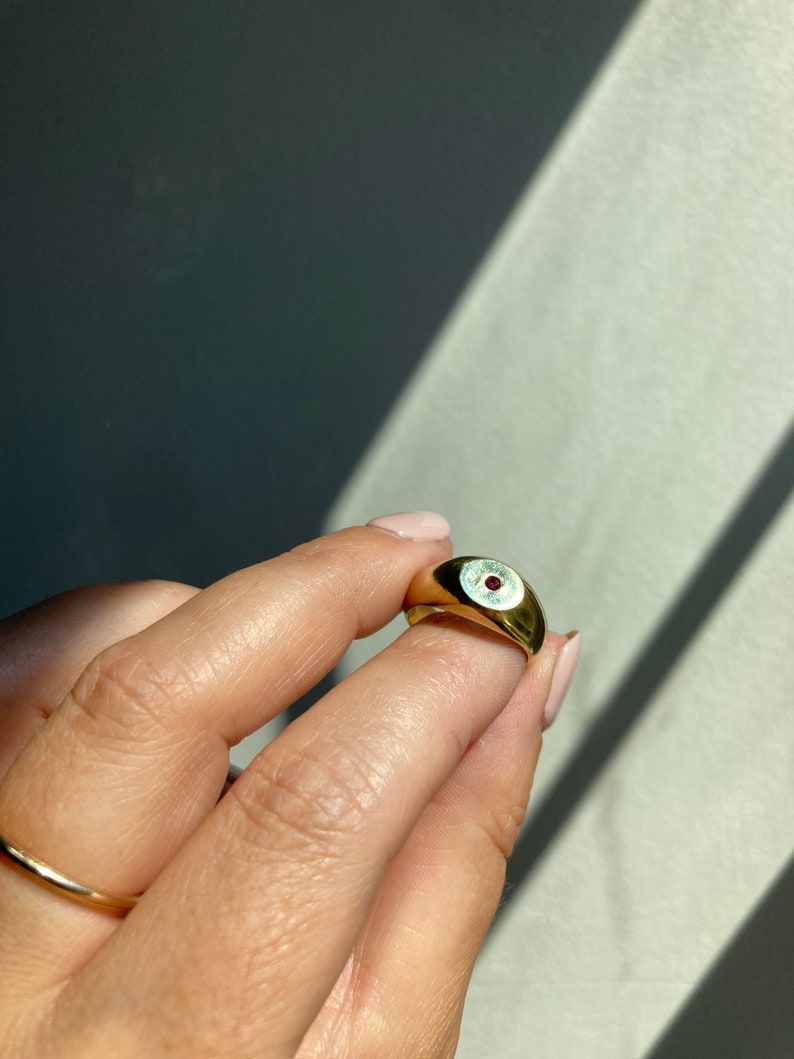 May include: A gold signet ring with a small red gemstone set in the center.