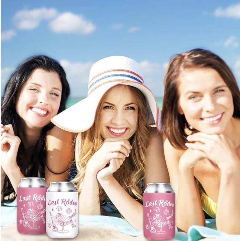 May include: Three women smiling on a beach with three pink and white can coolers. The coolers have the text "Last Rodeo" and a graphic of a person in a hammock with a guitar.
