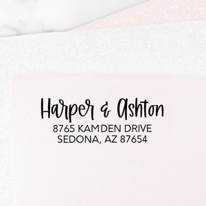 May include: A stack of three sheets of paper in shades of white and pink. The top sheet is pink and has black text that reads "Harper & Ashton" and an address. The other two sheets are white and have a glittery texture.