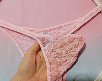 May include: Pink lace underwear with a delicate floral pattern. The underwear is hanging on a white hanger.