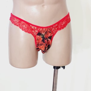 May include: Red lace thong underwear with a floral rose print on the front. The underwear has a delicate, feminine design with a low-rise waist and a comfortable fit. The floral print features red and orange roses.