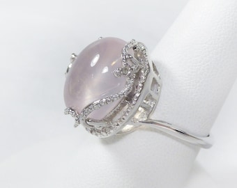 May include: A silver ring featuring a large, oval-shaped, pale pink gemstone set in a delicate, ornate design.
