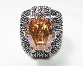 May include: A silver ring with a large, faceted, orange gemstone surrounded by a band of marcasite stones.