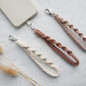 Könnte beinhalten: Drei Handy-Bänder in verschiedenen Farben und Texturen. Die Bänder sind aus geflochtenem Kordel und haben einen silbernen Metallverschluss. Die Bänder liegen auf einer hellgrauen Oberfläche.