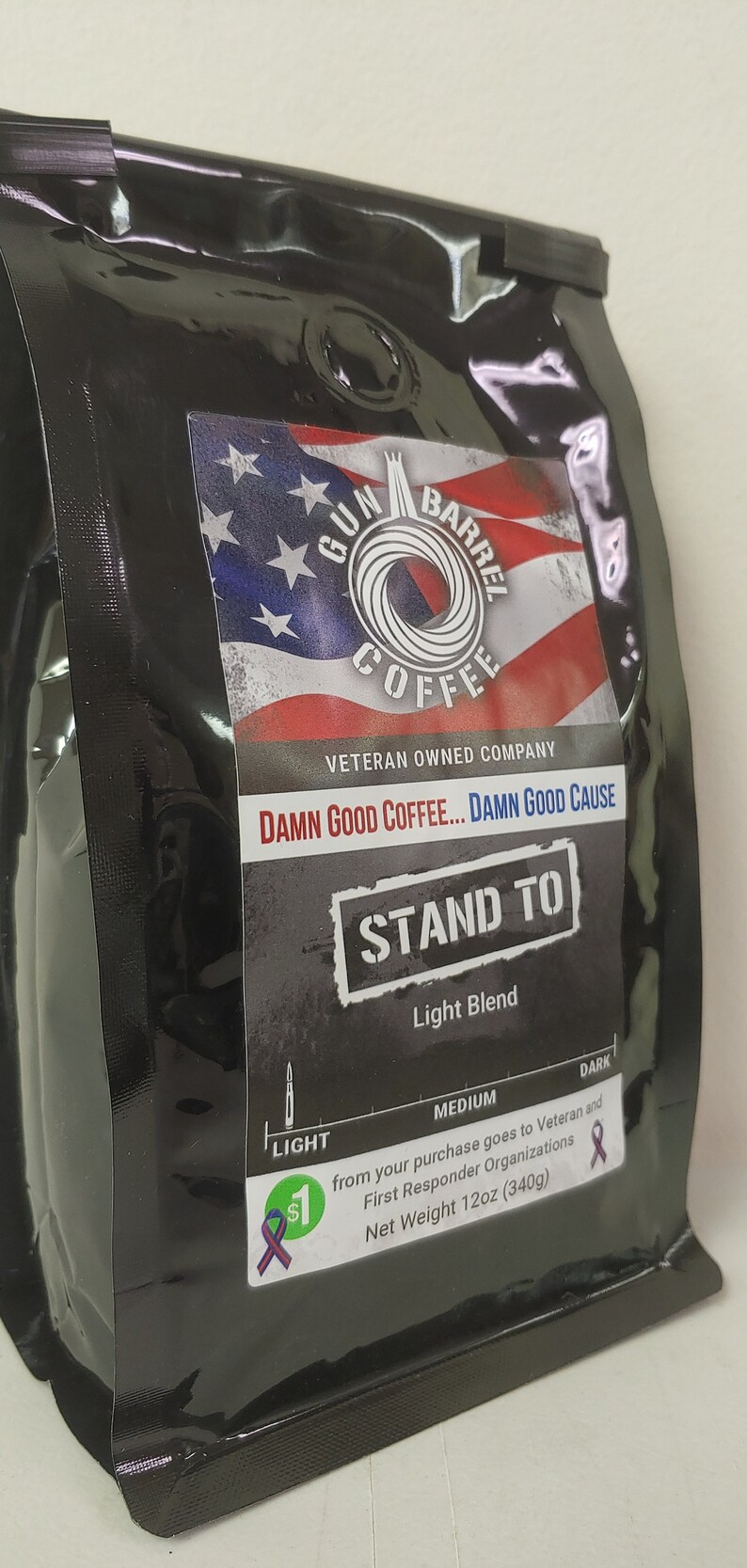 May include: A black coffee bag with a red, white and blue American flag design. The bag features the text "Gun Barrel Coffee", "Veteran Owned Company", "Damn Good Coffee... Damn Good Cause", "Stand To", "Light Blend", and "Net Weight 12oz (340g)".