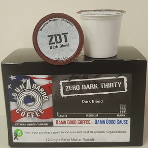 Könnte beinhalten: Eine Schachtel mit 12 einzeln portionierten Kaffeekapseln mit der Aufschrift "Zero Dark Thirty" Dark Blend. Die Schachtel ist schwarz mit einem rot-weiß-blauen amerikanischen Flaggenmuster. Die Kaffeekapseln sind mit "ZDT" Dark Blend beschriftet. Auf der Schachtel steht "Damn Good Coffee... Damn Good Cause" und dass ein Teil des Kaufpreises an Veteranen- und Ersthelferorganisationen geht.