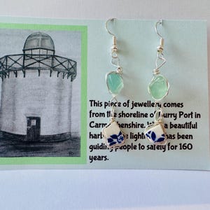 May include: Earrings with silver hooks, sea glass, and ceramic pieces with blue floral patterns. The card shows a lighthouse illustration and text: 'This piece of jewellery comes from the shoreline of Jurry Port'.