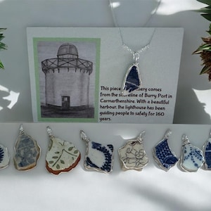 May include: Handmade pendants crafted from recycled ceramic pieces, featuring blue and white patterns. Each pendant is set in silver-coloured wire. A card with a lighthouse illustration and text about Burry Port is also shown.