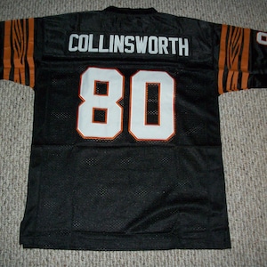 May include: Black football jersey with orange and white stripes on the sleeves. The back of the jersey has the name "COLLINSWORTH" and the number "80" in white with orange outlines.