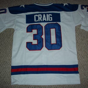 May include: White hockey jersey with blue and red trim. The back of the jersey has the name "CRAIG" and the number "30" in blue with white outlines.
