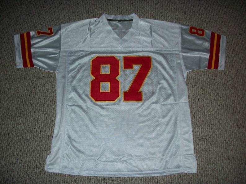 May include: White football jersey with red and gold trim. The number 87 is printed on the front in red with a gold outline.