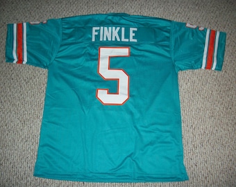 Könnte beinhalten: Ein türkisfarbenes Football-Trikot mit weißen und orangen Rändern. Auf der Rückseite des Trikots steht der Name "FINKLE" und die Nummer "5" in Weiß.