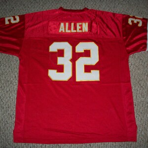 Puede incluir: Camiseta de f&uacute;tbol roja con ribetes blancos y dorados. El n&uacute;mero 32 est&aacute; en la espalda con el nombre "ALLEN" arriba.