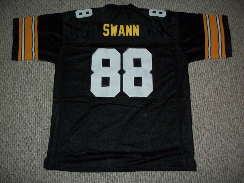 May include: Black football jersey with white and yellow stripes on the sleeves. The number 88 is on the back in white with the name "SWANN" in yellow above it.
