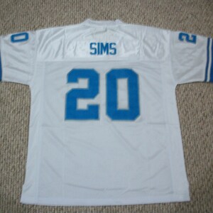 May include: White football jersey with blue and white stripes on the sleeves. The back of the jersey has the name "SIMS" and the number "20" in blue.