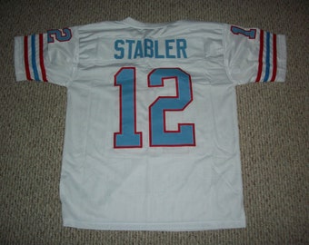Puede incluir: Camiseta de fútbol blanca con ribetes azules y rojos. La camiseta tiene el nombre "STABLER" y el número "12" en la espalda.