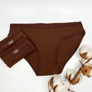Può includere: Tre paia di biancheria intima in cotone marrone con la parola "YOU" ricamata in vita.