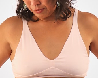 May include: A light pink, seamless, v-neck bra with adjustable straps.
