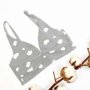 Puede incluir: Un bralette de algodón gris con estampado de nubes blancas. El bralette tiene un escote en V profundo y tirantes ajustables.