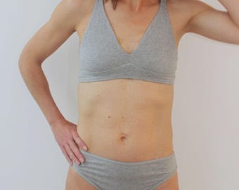 Könnte beinhalten: Ein hellgraues Baumwoll-BH- und Höschen-Set. Der BH hat einen V-Ausschnitt und einen Neckholder-Träger. Die Unterhose ist im Low-Rise-Stil gehalten. Das Set besteht aus einem weichen, bequemen Material.
