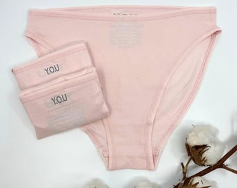 May include: Two pairs of pink cotton underwear with the word "YOU" printed on the waistband.