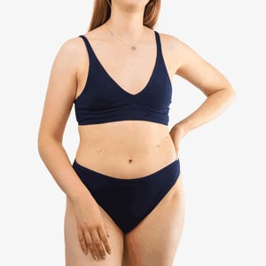 May include: Navy blue underwear set. The set includes a V-neck bralette and matching briefs. The bralette has thin straps and a gathered center. The briefs have a classic cut. The fabric appears to be a soft, solid color.