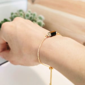 May include: A gold chain bracelet with a brown and black gemstone bead. The bracelet has a sliding clasp.