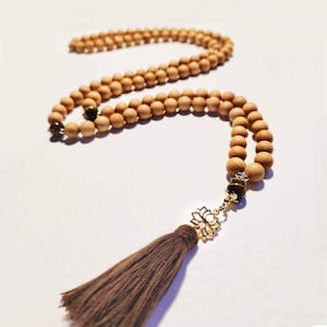 Op de afbeelding: Een bruine houten mala kralenketting met een gouden lotus bedel en een bruine kwast. De ketting heeft tijgeroog kralen.