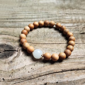 May include: A wooden bead bracelet with a white gemstone charm. The bracelet is made of natural wood beads and has a simple, elegant design.