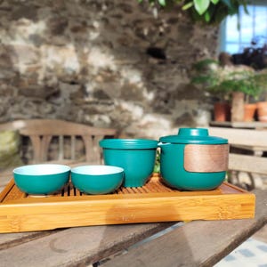 May include: A teal green tea set with a teapot, a small pitcher, and two cups. The set is on a bamboo tray.