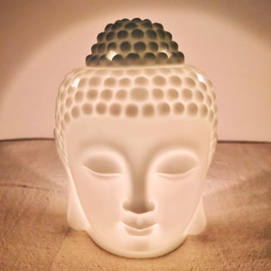 Puede incluir: Difusor de cabeza de Buda de cerámica blanca con una superficie texturizada y una pequeña abertura en la parte superior para aceites esenciales o ceras fundidas.