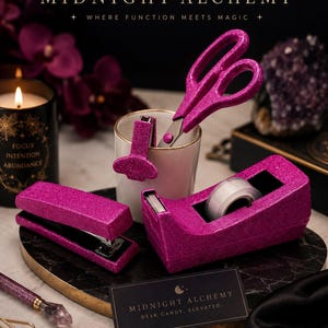May include: A selection of magenta glitter desk accessories, including scissors, a stapler, tape dispenser, and a paper clip holder. The image also features a candle, a pen, and a business card with the text "MIDNIGHT ALCHEMY".