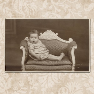 Mignon bébé sur un mini canapé - Carte postale photo édouardienne antique du début des années 1900.