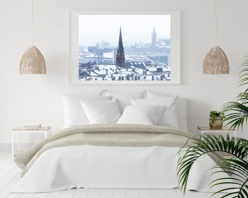 May include: A white bedroom with a bed, two bedside tables, and a framed photograph of a snowy city skyline. The photograph shows a tall church steeple in the centre of the image.