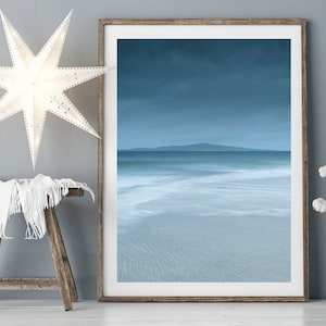 Puede incluir: Una impresión enmarcada de un paisaje marino en tonos azules y blancos. La imagen representa un océano borroso con una isla distante bajo un cielo nublado. Una linterna de papel blanca en forma de estrella cuelga del techo.