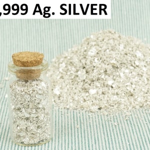 Könnte beinhalten: Ein Glasgefäß mit einem Korkverschluss, gefüllt mit Silberflocken. Das Gefäß steht auf einer blau-weiß gestreiften Oberfläche. Der Text "99,999 Ag. SILVER" ist über dem Gefäß sichtbar.