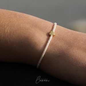 May include: A white beaded bracelet with a gold heart charm.