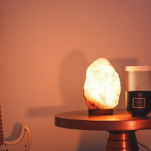 May include: A warm, glowing Himalayan salt lamp sits on a copper-colored table next to a black candle and a gray speaker labeled "SOHO".