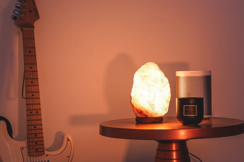 May include: A warm, glowing Himalayan salt lamp sits on a copper-colored table next to a black candle and a gray speaker labeled "SOHO".