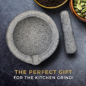 May include: A grey stone mortar and pestle set. The mortar is round and has a textured surface. The pestle is long and cylindrical. The set is on a grey background.