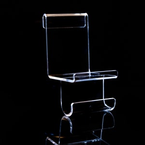 May include: A clear acrylic display stand with two shelves. The stand is designed to hold small items, such as jewellery or figurines.